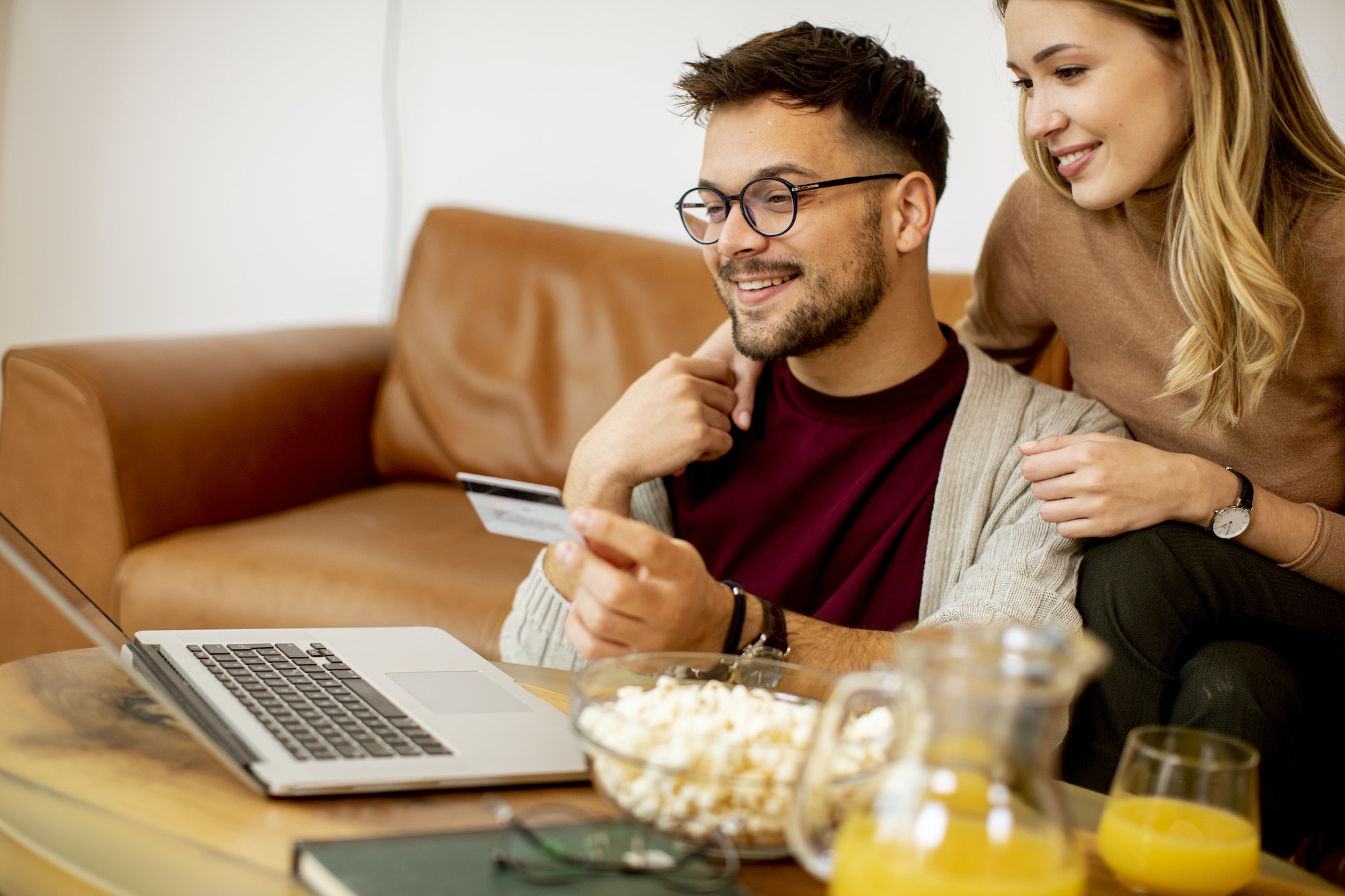 Young woman and young man using laptop for onlin payment while sitting by sofa at home